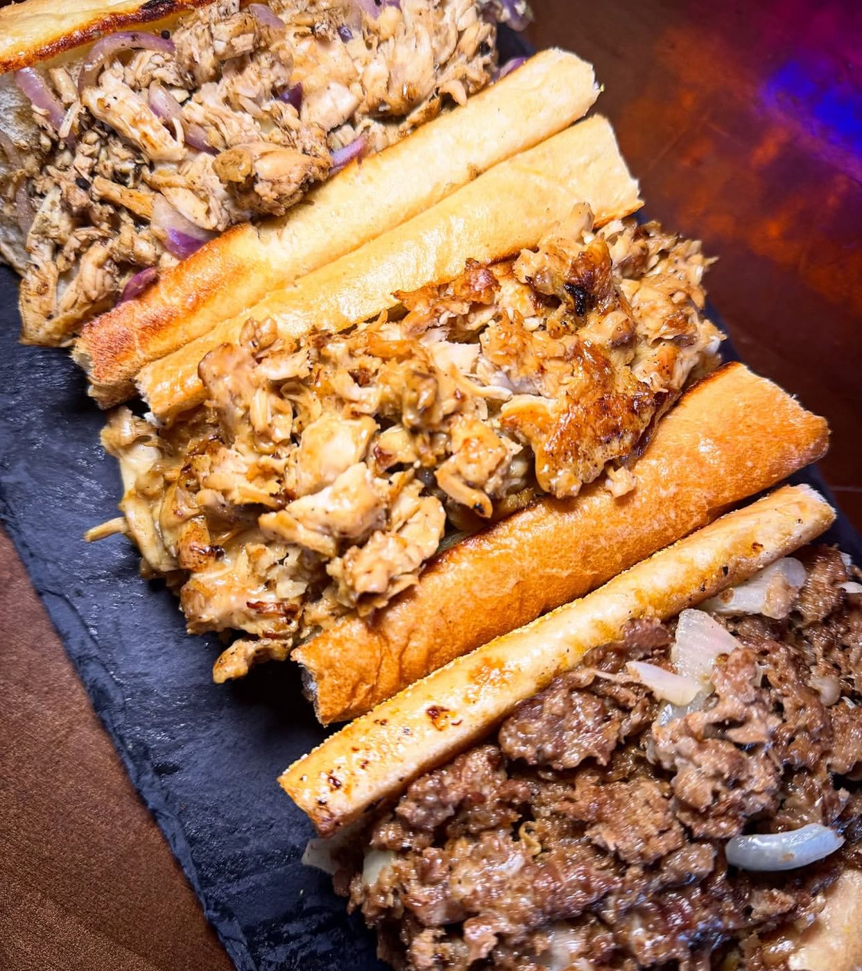 Three Urban cheesesteaks on a slate board